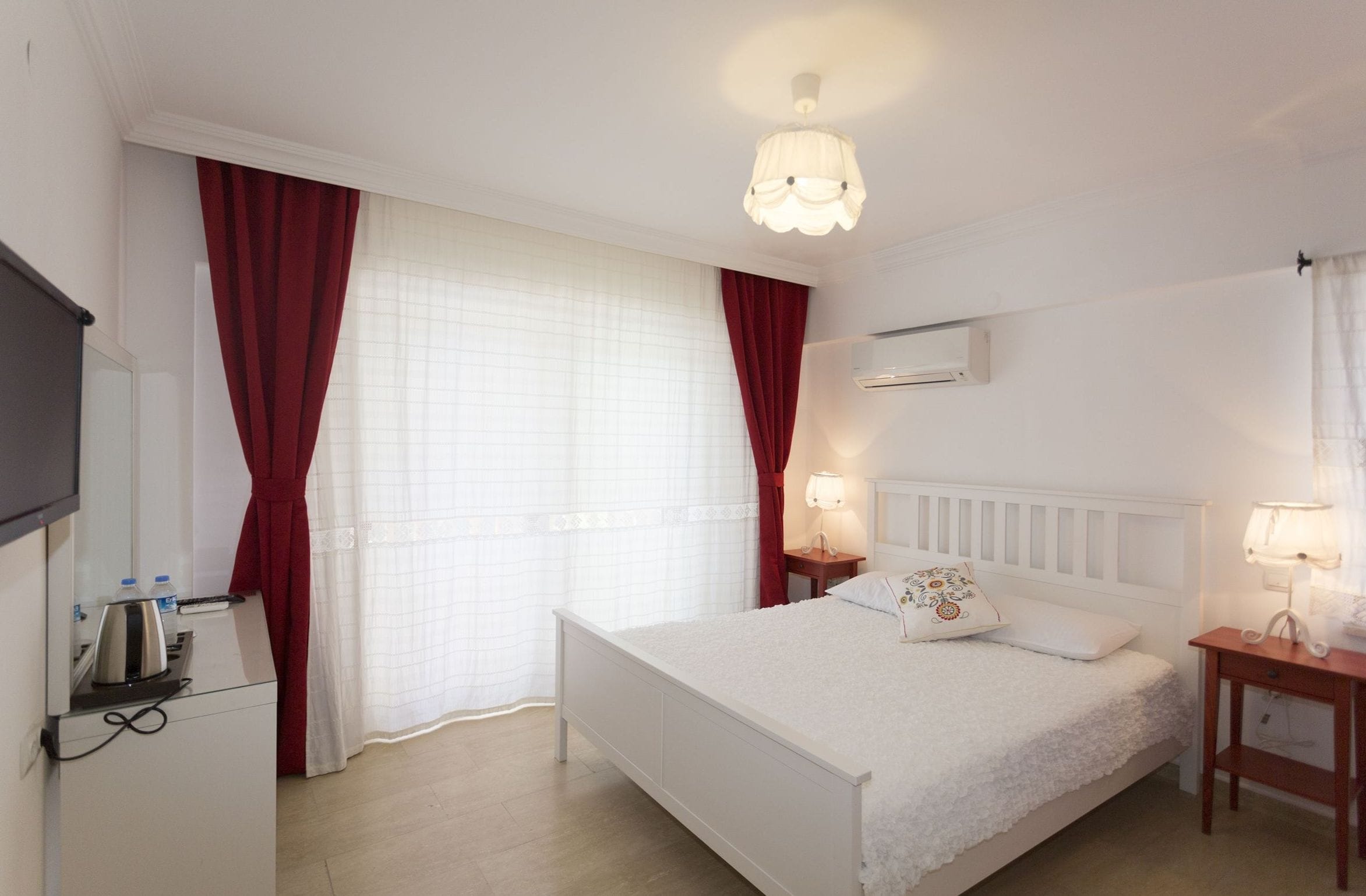 A hotel room with a bed, bedside tables, a TV, and a window with curtains.