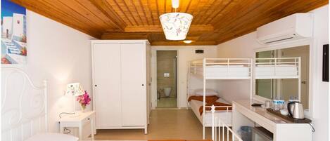 Une chambre d’hôtel compacte avec un plafond en bois, un lit simple, un bureau avec une lampe, un lit superposé et une kitchenette.
