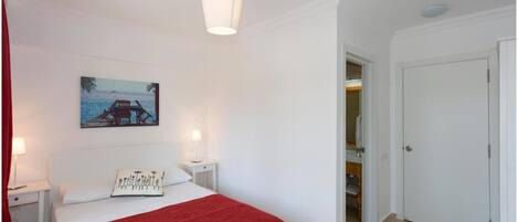 Un dormitorio con cama, mesita de noche, lámpara, un cuadro y una puerta.