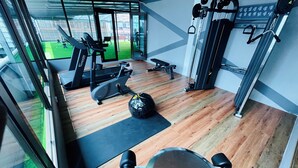Un gimnasio con equipo de ejercicio, una cinta de correr y vistas a un espacio verde al aire libre.
