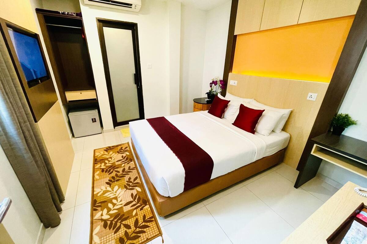 Een hotelkamer met een bed, een nachtkastje met een plant, een spiegel en een deur.