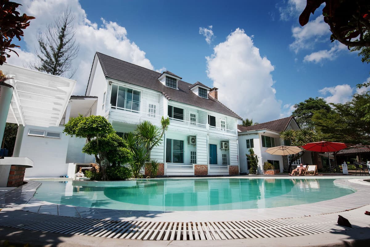 Une maison à deux étages avec une piscine, entourée d’arbres et sous un ciel dégagé.