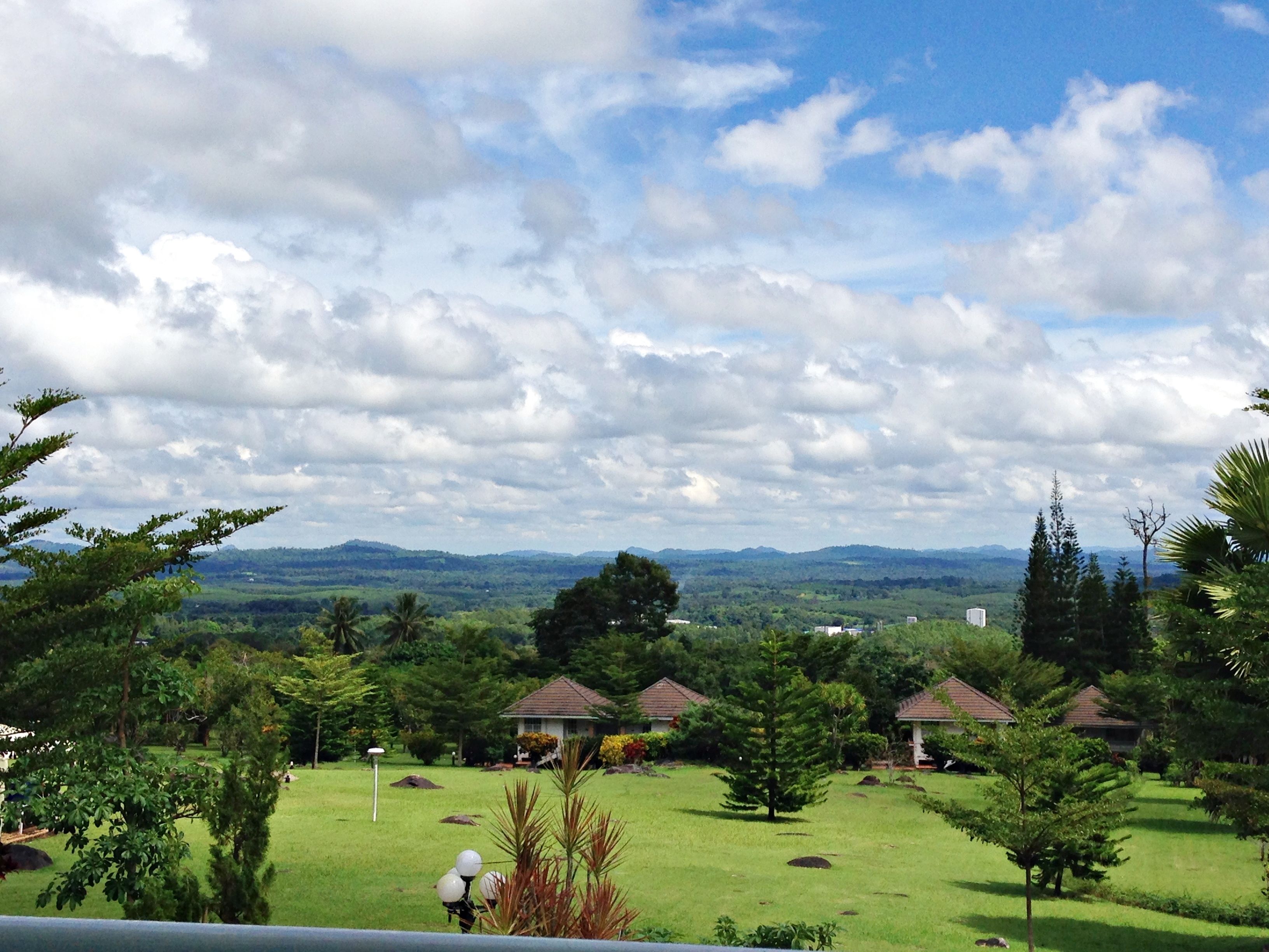 A view of a residential area with houses, a grassy field, and a distant mountain range under a cloudy sky.