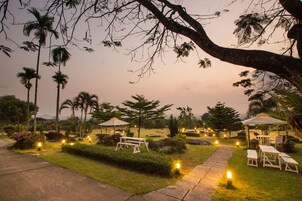 A garden area with pathways, benches, and tables under umbrellas, surrounded by palm trees and greenery.
