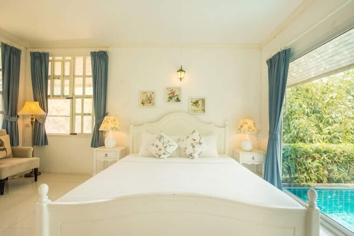 Une chambre à coucher comprenant un lit, des tables de chevet, une commode, une lampe, une chaise et une fenêtre avec des rideaux.