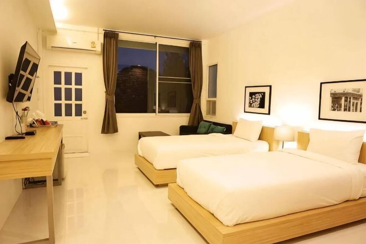 Une chambre d’hôtel avec deux lits, un bureau, une chaise, une télévision et une fenêtre avec des rideaux.