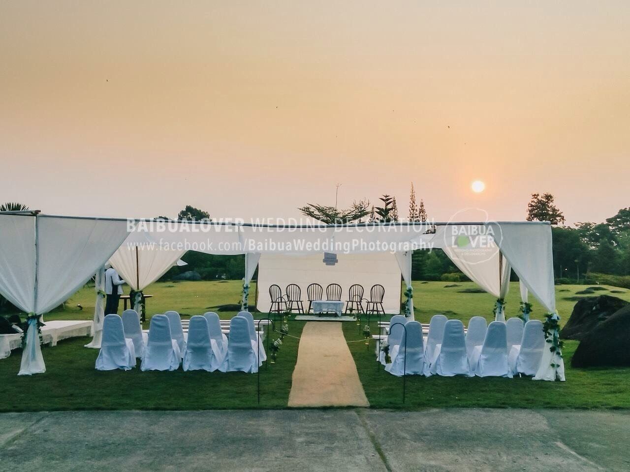 An outdoor wedding setup with a white archway, chairs, and a pathway leading to the ceremony area.