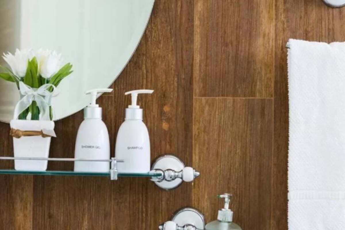 A bathroom with a wooden wall, a glass shelf holding toiletries, and a white towel.