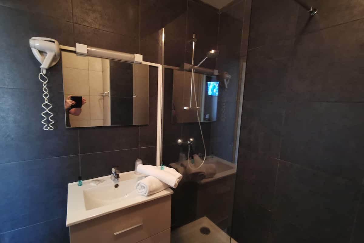 Ein modernes Badezimmer mit einem weißen Waschbecken, einem Spiegel, einem Fön und einer Duschkabine.