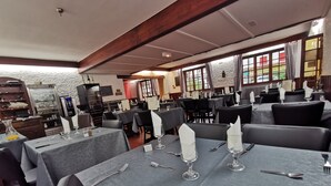 Een restaurant met gedekte tafels, met een stenen muur en houten balken.