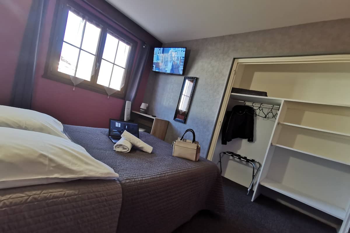 Ein Hotelzimmer mit einem Bett, einem Fernseher, einem Schreibtisch mit einem Laptop, einem Kleiderschrank und einem Fenster mit Vorhängen.