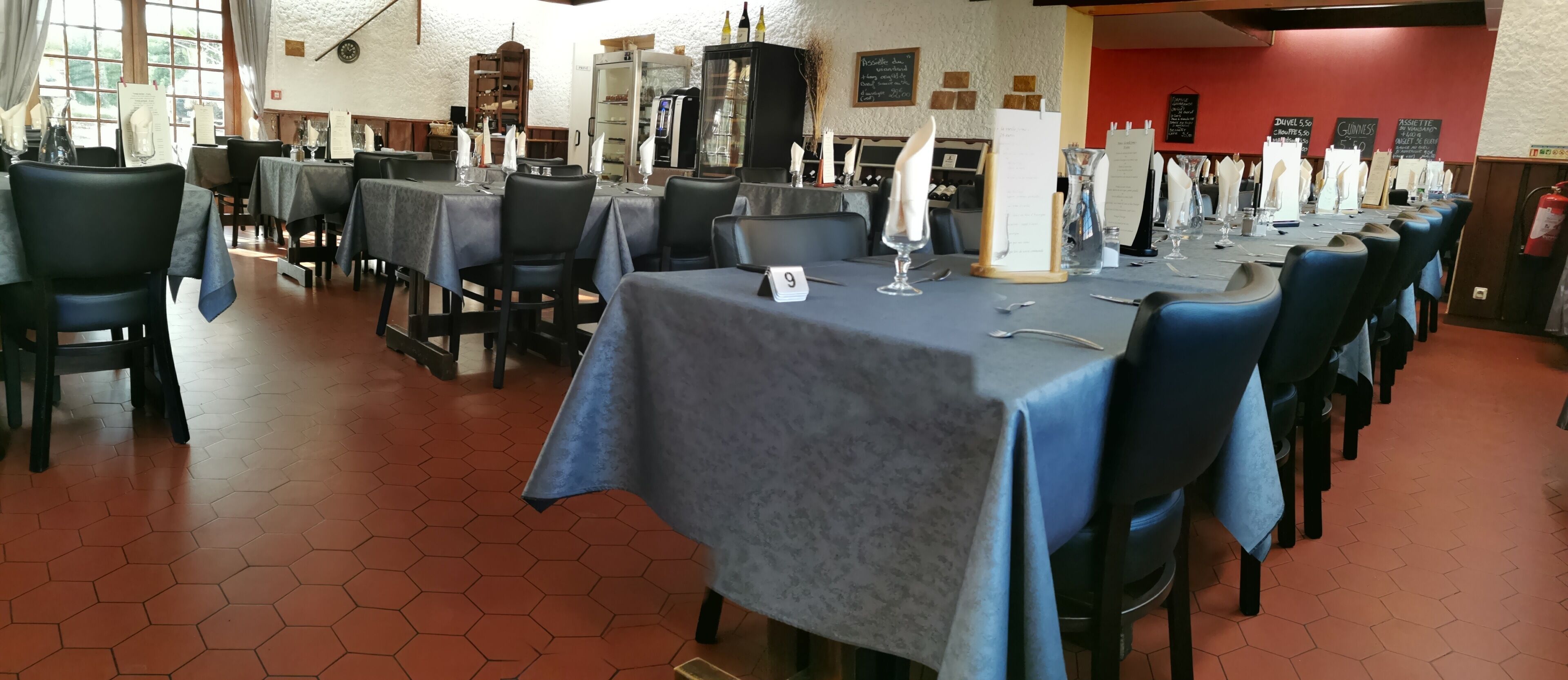 A restaurant with hexagonal tiled flooring, tables set with white napkins, and a menu board on the wall.