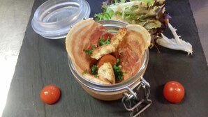 Een maaltijd met een glazen bakje, inclusief brood, tomaten en peterselie, op een donker oppervlak, met een salade en twee tomaten ernaast.