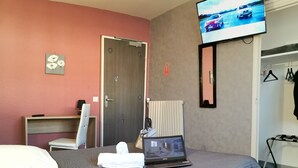 Een hotelkamer met een bed, een bureau, een stoel, een laptop en een televisie aan de muur.