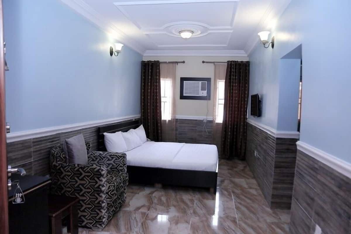 A bedroom with a bed, a sofa, a TV, and a window with curtains.