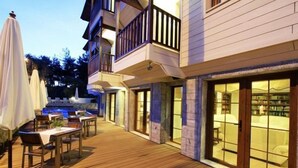A wooden deck with outdoor seating and a pool, connected to a building with large windows and a balcony. - Summer Otel (Ula)
