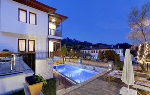 Un edificio de dos plantas con piscina, asientos exteriores y un balcón.