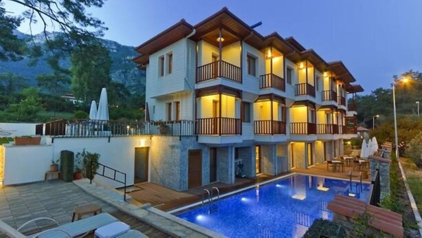 A multi-story hotel with a swimming pool, outdoor seating, and a mountainous backdrop. - Summer Otel (Ula)