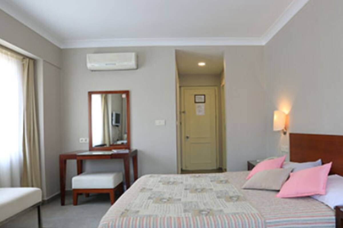 Une chambre d’hôtel comprenant un lit, un bureau, une chaise, un miroir, une porte et un climatiseur fixé au mur.
