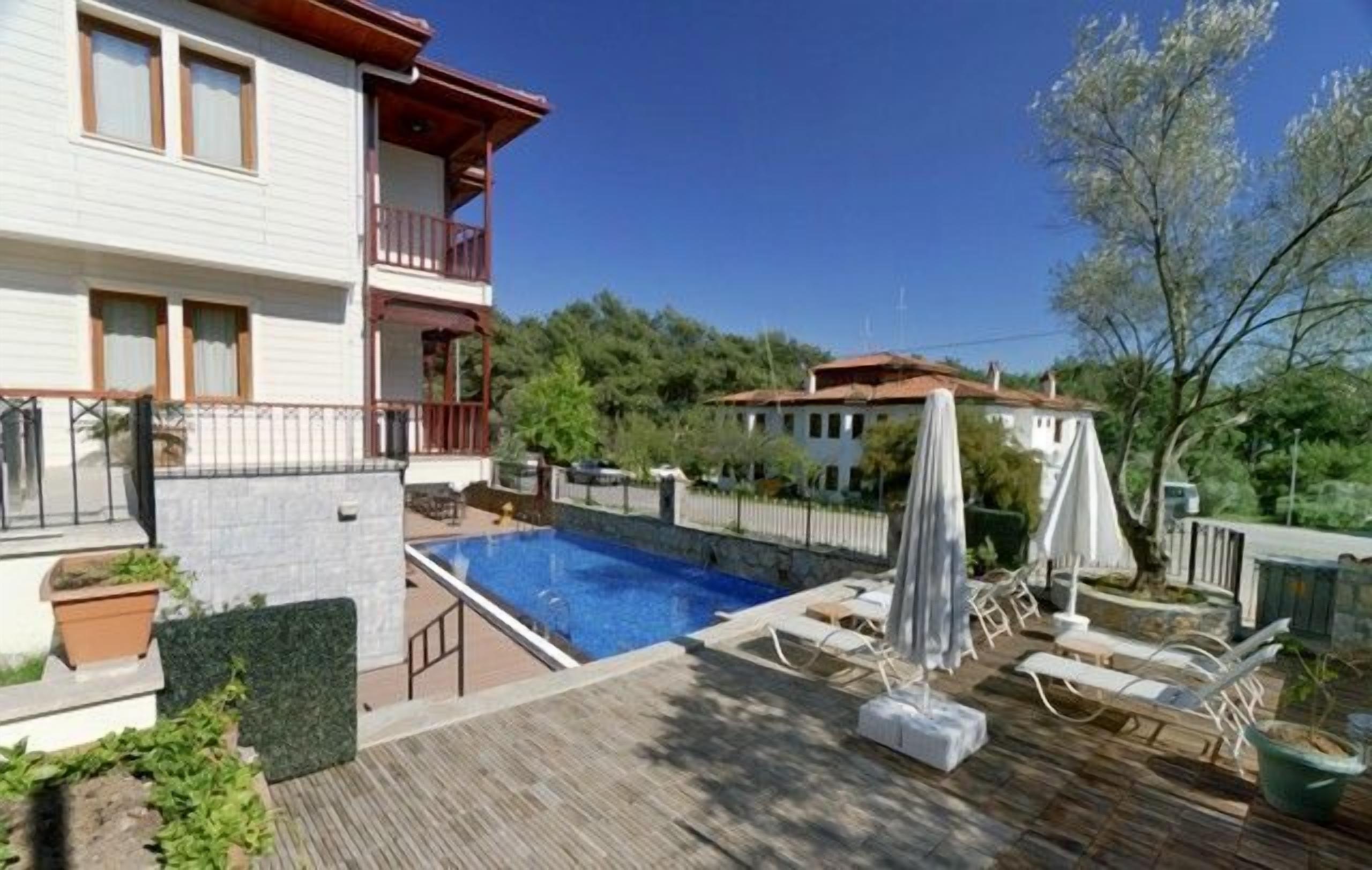 Un edificio de dos pisos con piscina, mobiliario exterior y vista a un área boscosa.