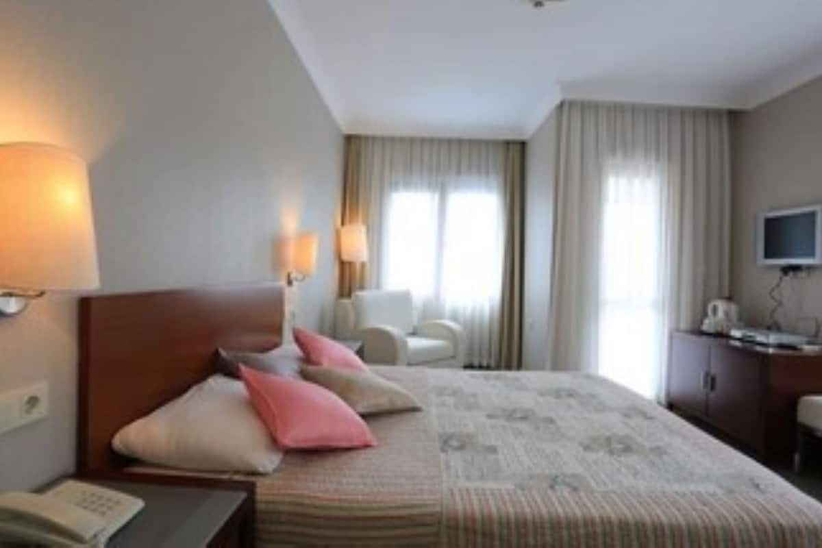 Une chambre d’hôtel comprenant un lit, des lampes de chevet, un bureau avec un téléphone, une télévision et une fenêtre avec des rideaux.