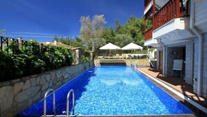 A swimming pool with a stone wall on one side and a building with outdoor seating on the other. - Summer Otel (Ula)