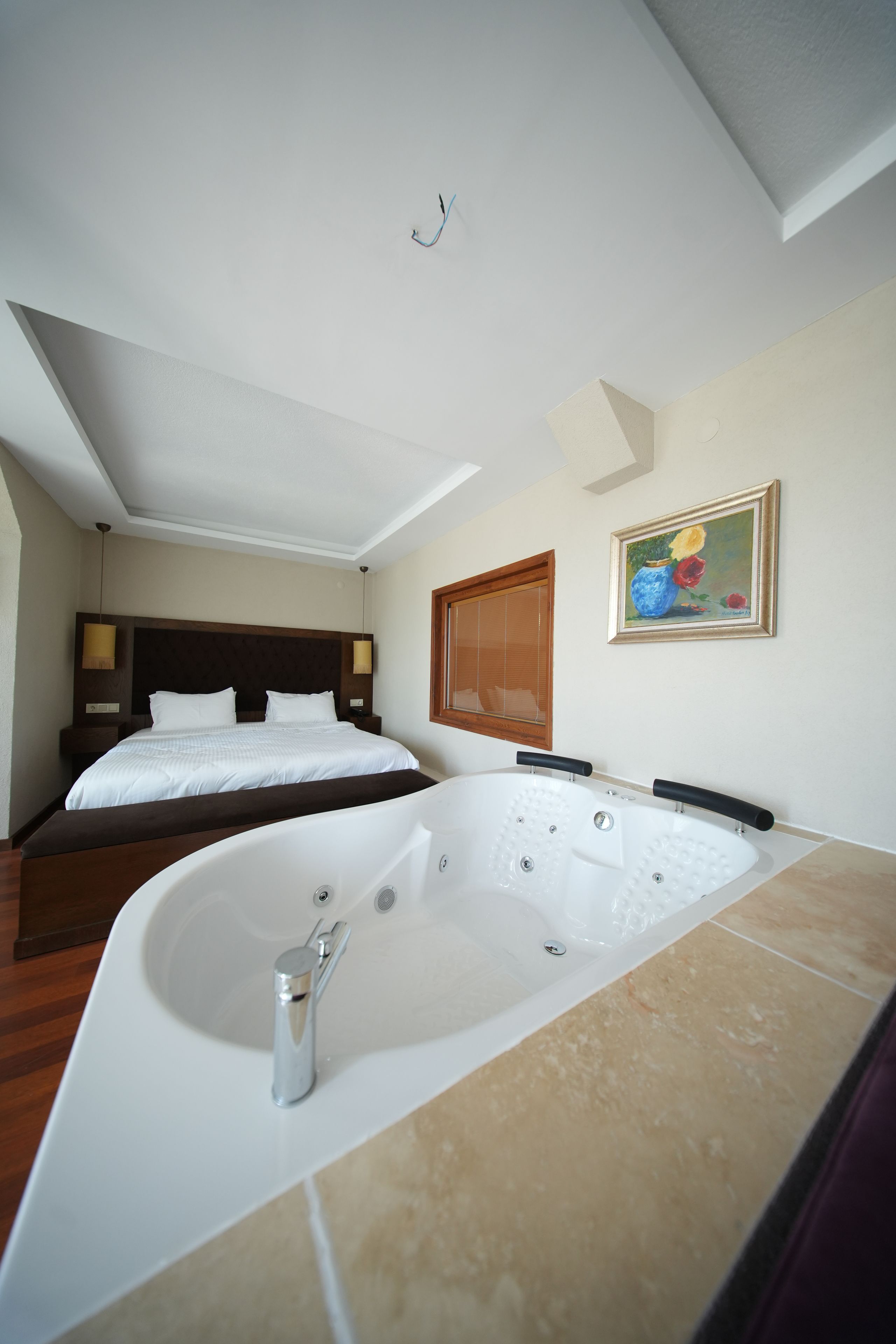 A hotel room with a large bathtub, a double bed, and a painting on the wall.