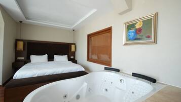 A hotel room with a large bathtub, a double bed, and a painting on the wall.