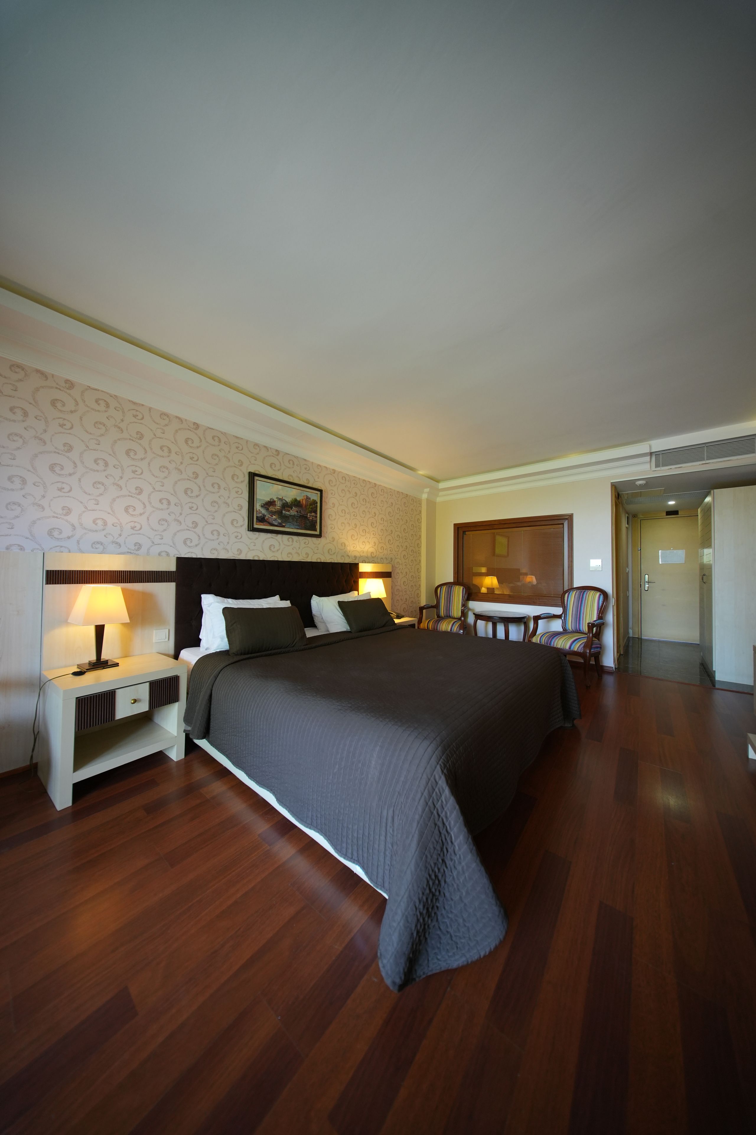 Una habitación de hotel con una cama grande, una mesita de noche con lámpara, una silla y una pequeña mesa.
