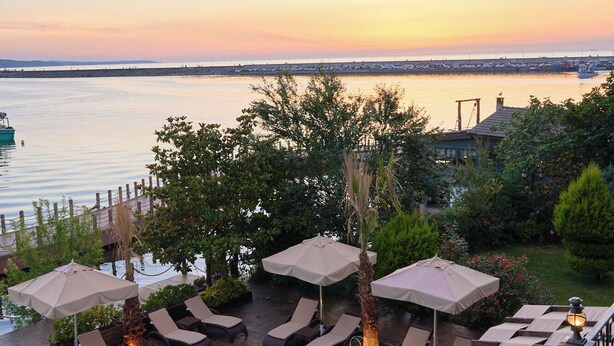 A pool area with lounge chairs and umbrellas, overlooking a body of water with a sunset in the background.