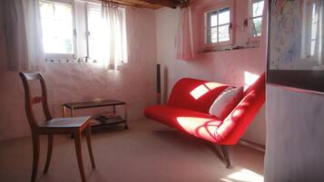 Una habitación con techo de madera, un sofá rojo, una silla de madera, una mesita pequeña y un refrigerador.