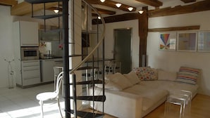Un espacio moderno para vivir con una escalera espiral, un conjunto de sofás y una zona de cocina.