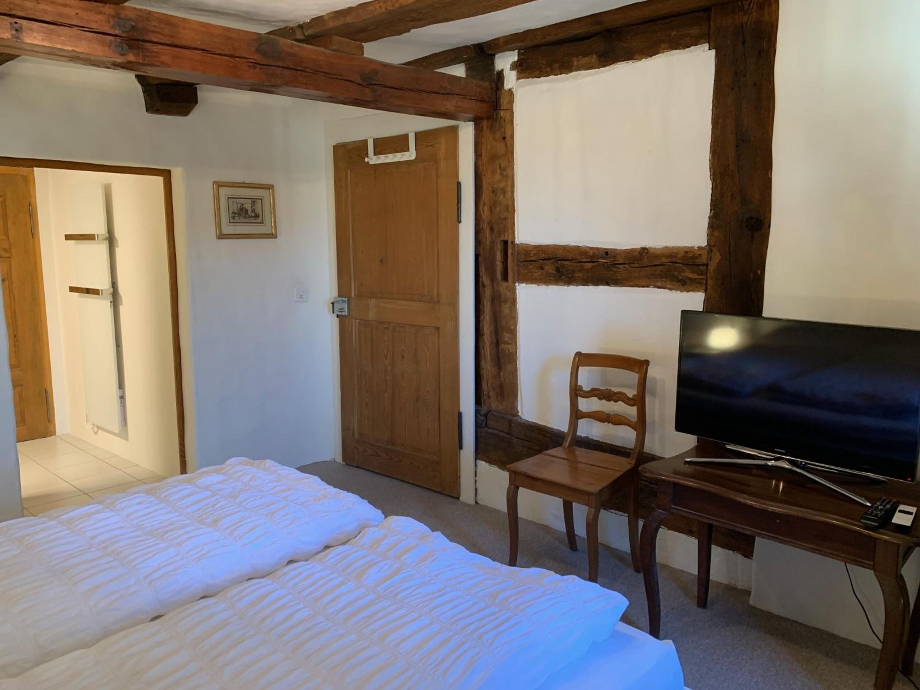 Une chambre à coucher avec un lit, une télévision, une chaise et des poutres en bois au plafond.