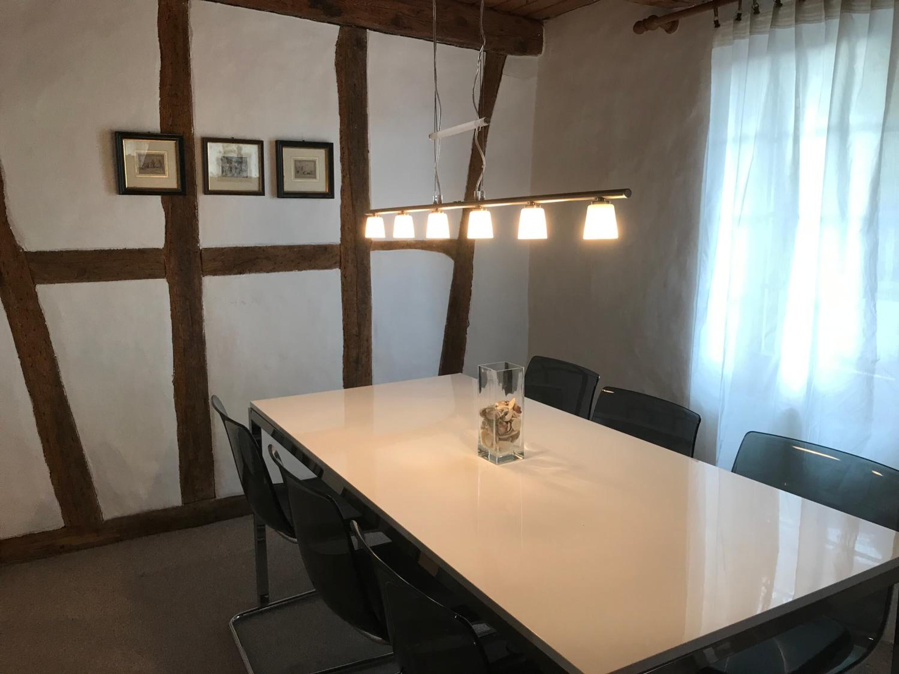 A conference room with a long table, black chairs, framed pictures on the wall, and a hanging light fixture.