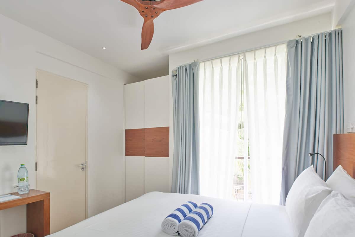 A hotel room with a bed, a wooden headboard, a television on the wall, and a window with curtains.