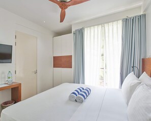 Habitació d'hotel amb un llit, un panell de fusta al capçal, una televisió penjada a la paret i una finestra amb cortines.
