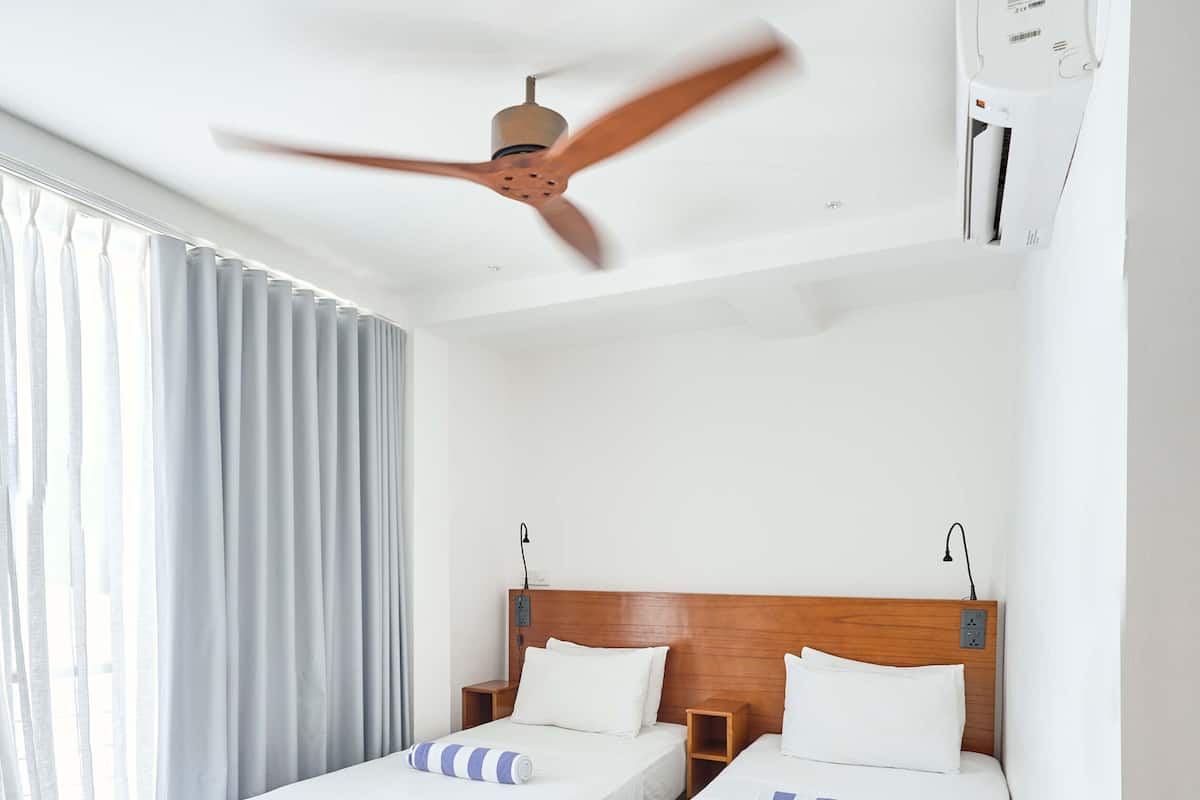 A hotel room with two wooden beds, white bedding, a ceiling fan, and a window with curtains.