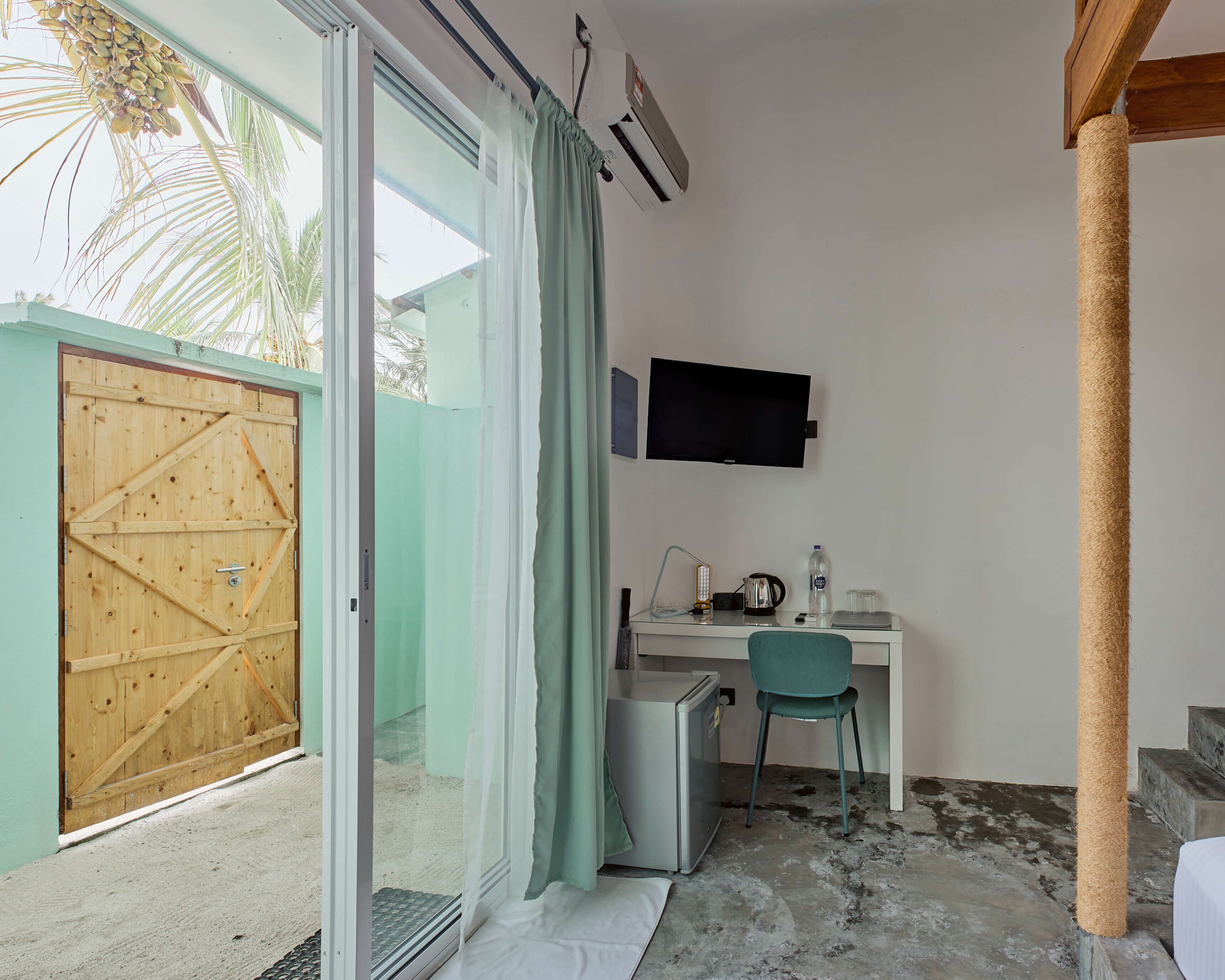 A room with a wooden door, a desk with a chair, a television, and a small refrigerator.