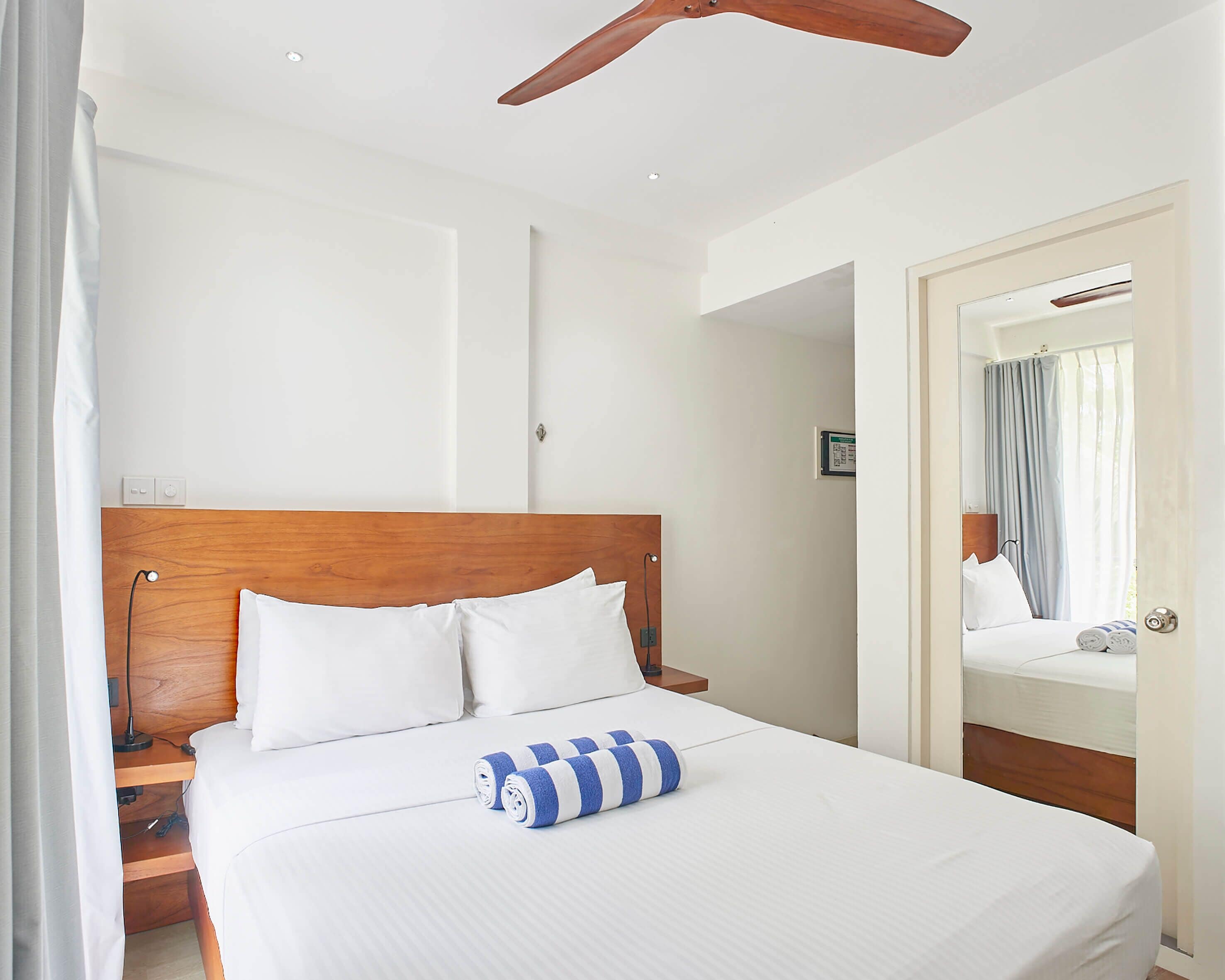 A hotel room with a wooden headboard, white bedding, and a ceiling fan.
