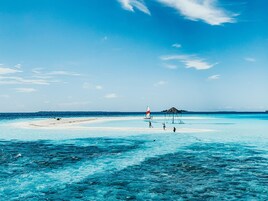 A beach with clear turquoise waters, a small hut, and a sailboat.