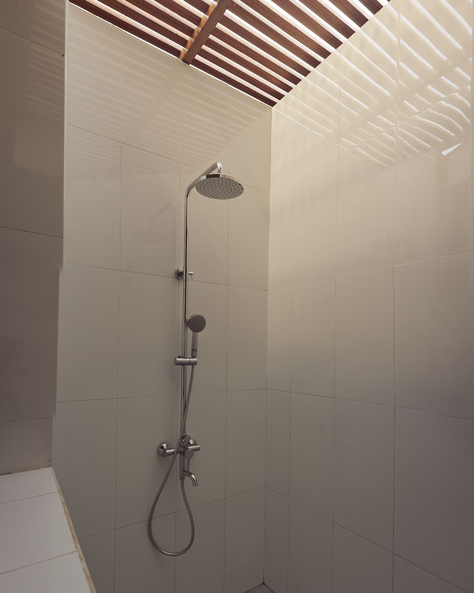 Eine moderne Dusche mit Handbrause und Regendusche, an einer Wand mit Holzdielen Decke befestigt.