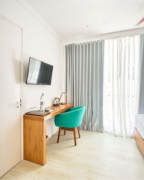 Habitació d'hotel amb escriptori de fusta, cadira color turquesa, televisió de pantalla plana i finestra gran amb cortines.