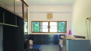 A narrow kitchen with dark cabinets, a window, and a refrigerator. - Chomlay Restaurant & Room for Rent (Rayong)