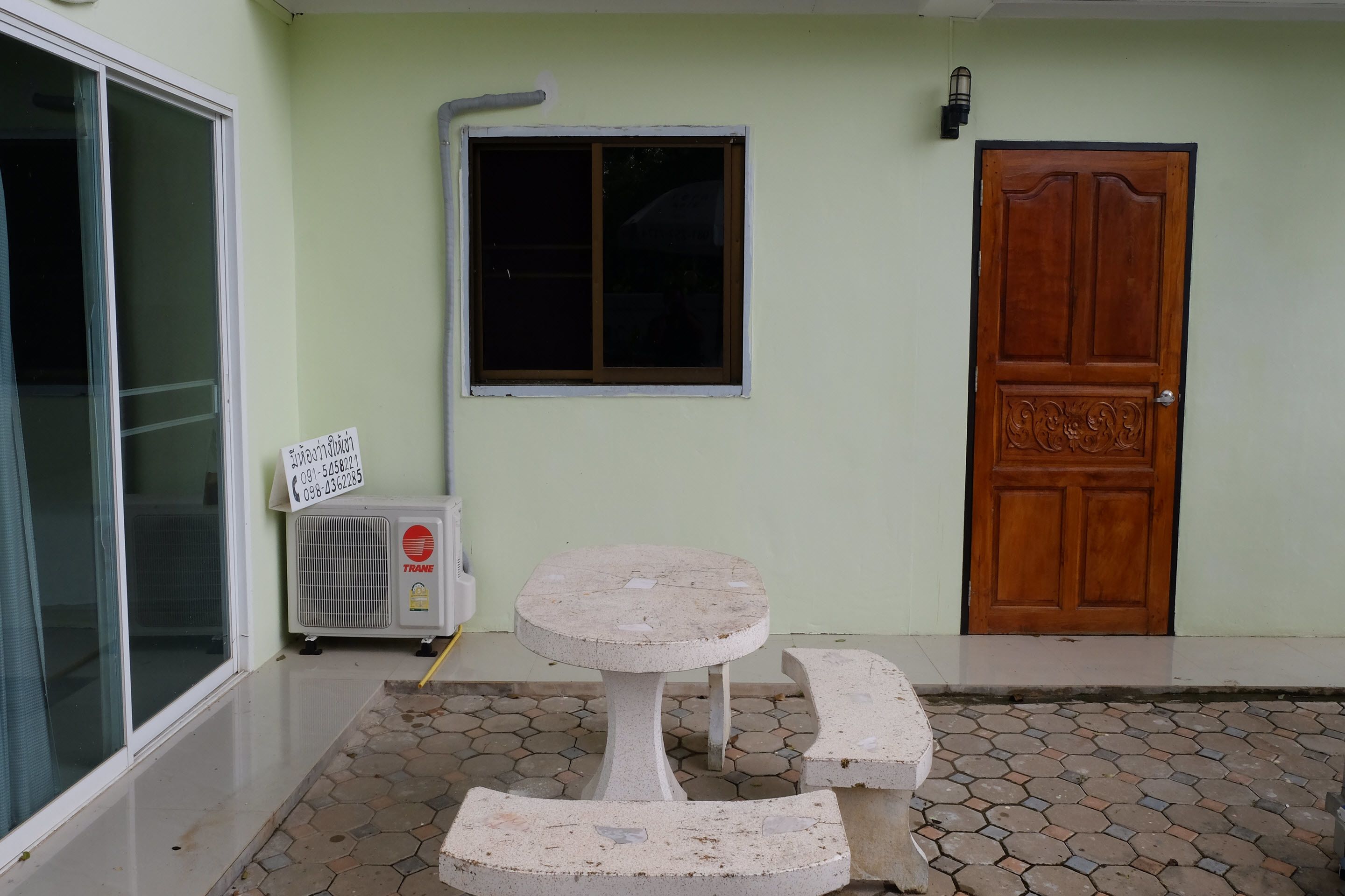 A small outdoor seating area with a table and benches, a window, a door, and an air conditioning unit.