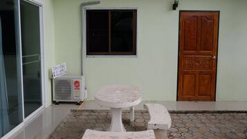 A small outdoor seating area with a table and benches, a window, a door, and an air conditioning unit.