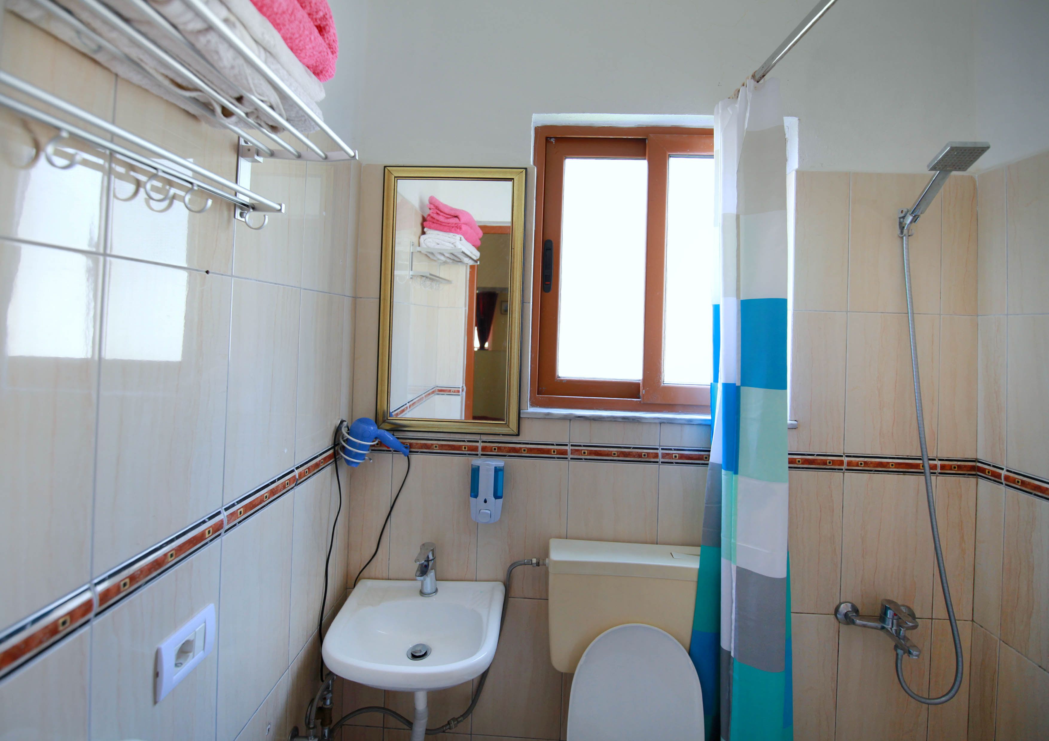 A bathroom with a sink, toilet, and shower. There is a window above the toilet and a towel rack above the sink.