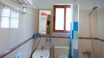 A bathroom with a sink, toilet, and shower. There is a window above the toilet and a towel rack above the sink.