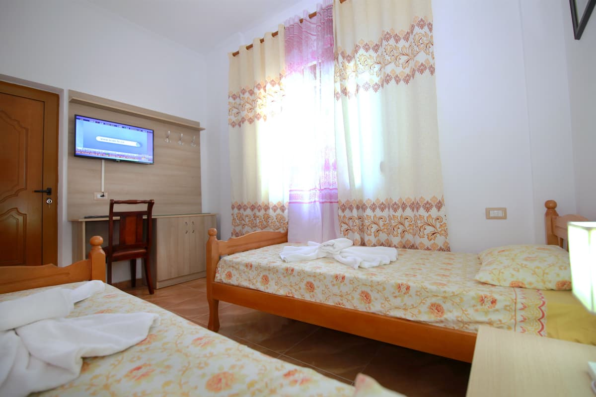Una habitación de hotel con dos camas individuales, un escritorio de madera, un televisor y una ventana con cortinas.