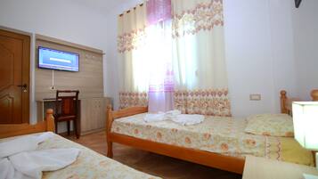 Hotellihuone, jossa on kaksi erillistä sänkyä, puinen työpöytä, televisio ja ikkuna, jossa on verhot.