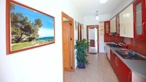 A kitchen with red cabinets, a sink, and a stove. There is a potted plant and a framed picture on the wall.